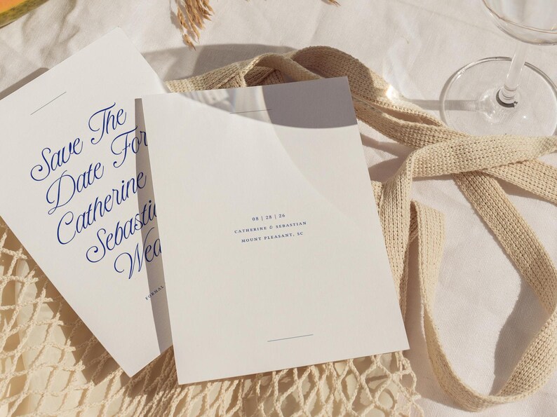 May include: A white save the date card with blue calligraphy text that reads "Save the Date for Catherine & Sebastian Wedding". The date is printed in blue text below: "08 | 28 | 24 Catherine & Sebastian Mount Pleasant, SC"