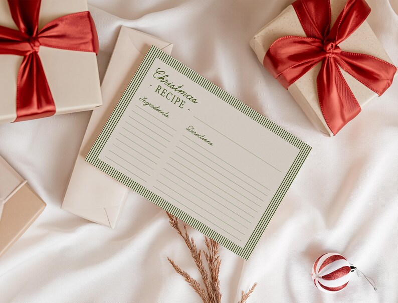 May include: A cream-colored recipe card with green striped borders and the text "Christmas RECIPE" is displayed. Two wrapped gifts with red satin bows and a decorative ornament are also present, all on a white satin surface.