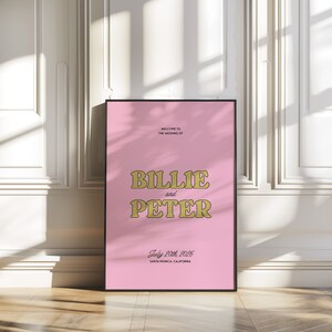 K&ouml;nnte beinhalten: Rosa Hochzeitseinladung mit goldener Schrift. Es steht "Willkommen zur Hochzeit von Billie und Peter. 20. Juli 2025. Santa Monica, Kalifornien."