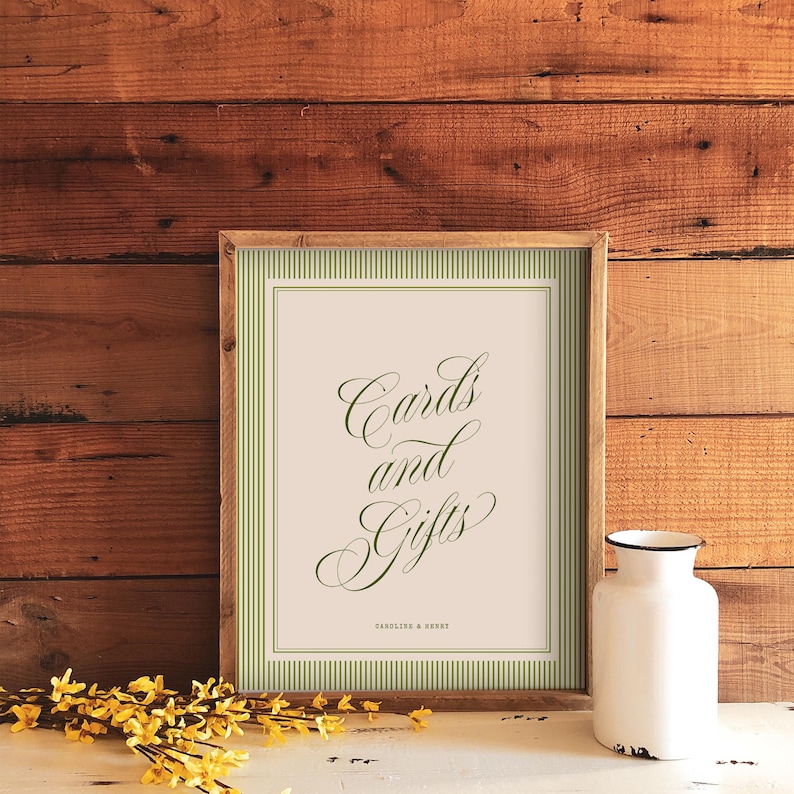 May include: A rectangular wooden frame containing a sign with a cream background, green vertical stripes, and green cursive text that reads Cards and Gifts, with the smaller text Caroline & Henry printed at the bottom of the sign.