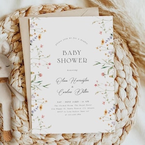 May include: A white baby shower invitation with a floral border. The text reads "Please join us for a double baby shower honoring Olivia Harrington & Caroline Dutton. Sat June 24th 11 AM The Orchid Room The Royal Hotel 234 Happy St. Santa Monica, CA 90201 RSVP to [phone number] before June 1st"
