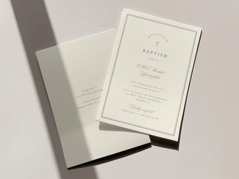 May include: Two off-white baptism invitations with elegant gold text and a cross symbol. One invitation is open, revealing the event details, while the other is closed. The invitations are on a light-colored surface.
