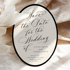 May include: An oval-shaped wedding save the date card with a black border on a cream background. The text reads: Have the Date for the Wedding of Eloise Smith and Henry Pierce, July 20, 2027, Huntington, New York. Formal invitation to follow.