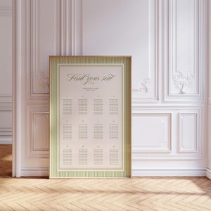 May include: A framed seating chart with the text "Find your seat" in elegant script. The chart has a cream background with green striped borders and a gold frame. The background is a white wall with decorative molding.