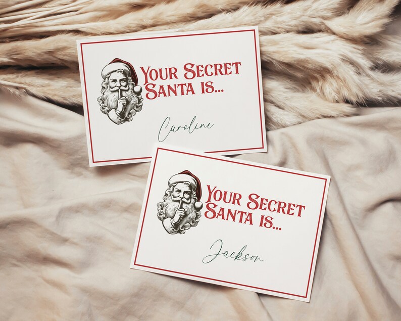 May include: Two white cards with red borders and a Santa Claus illustration. The text on the cards reads "Your Secret Santa is..." followed by a name. The first card says "Caroline" and the second card says "Jackson".