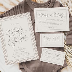 Puede incluir: Una invitación a un baby shower y sus complementos se muestran sobre un body acanalado color topo. La invitación dice "Baby Shower" en una elegante escritura. Las tarjetas adicionales incluyen detalles de "Books for Baby" y "Diaper Raffle".