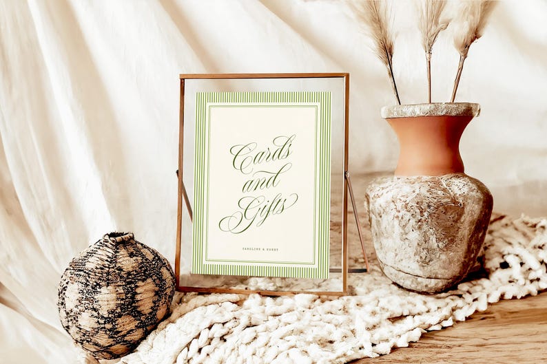 May include: A rectangular glass frame with a thin copper border containing a cream-colored sign with green pinstriped borders. The sign features the dark green cursive text "Cards and Gifts" above the smaller text "Jocelyn & David".