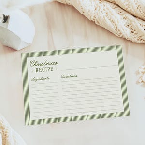 May include: A cream-colored recipe card with green striped borders and the words "Christmas Recipe" in elegant script. The card has spaces for ingredients and directions, perfect for holiday baking. A cozy, cream-colored knitted blanket and decorative vase are in the background.