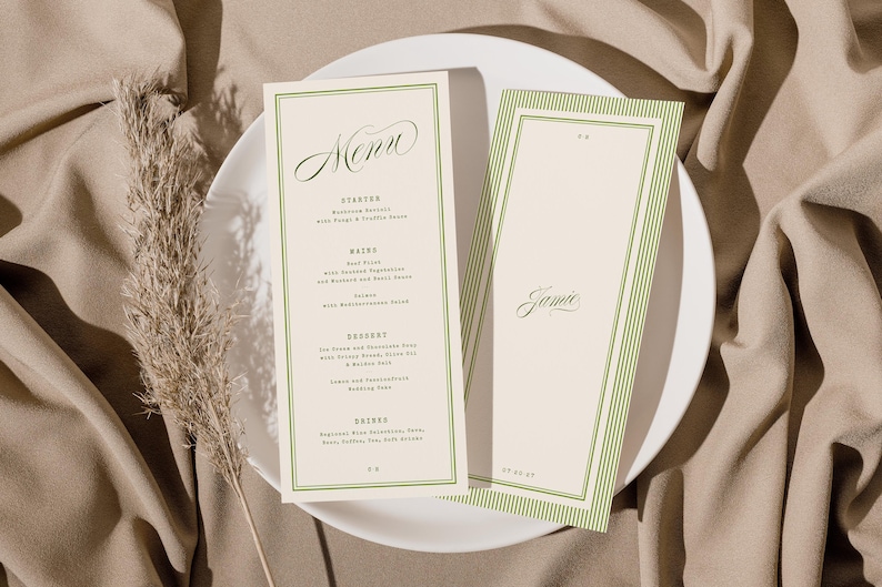 May include: Two cream-coloured menu cards with green borders and text, one labelled "Menu" and the other "Jamie", rest on a white plate. The background is a beige fabric with a dried plant.