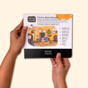 Peut inclure: Un carnet de croquis noir avec le texte "Viviva Sketchbook" et "Viviva Colors" sur la couverture. La couverture pr&eacute;sente une illustration d'une femme assise sur une chaise dans une pi&egrave;ce avec une plante, une lampe et une fen&ecirc;tre. Le texte sur la couverture comprend &eacute;galement "Premium Handmade Sketchbooks", "Carnets de Croquis Premium Faits &agrave; la Main", "Cuadernos de Bocetos Hechos a Mano de Primera Calidad", "AS Cotton/Coton A5/Algod&oacute;n A5", et des d&eacute;tails sur le papier, y compris le poids, la taille et le type.