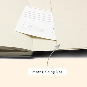 Peut inclure: Un carnet noir avec une fente pour papier sur la reliure. La fente est con&ccedil;ue pour contenir un morceau de papier, comme une carte postale ou une note.