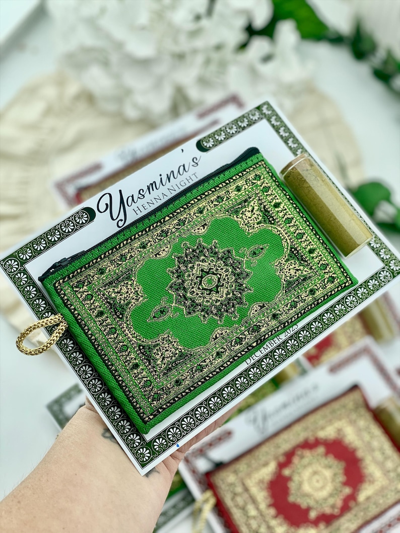 A hand holds up a green patterned mini wallet favor set, with a henna tube and a personalized card visible.