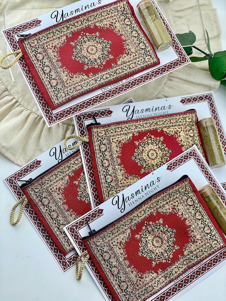 Four red patterned mini wallet favor sets are arranged on a white surface, each with a henna tube and a personalized card.