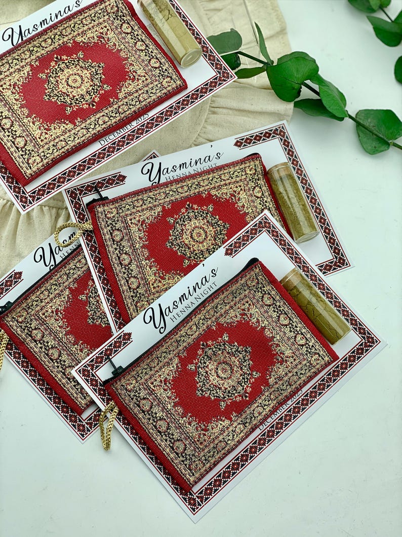 Four red patterned mini wallet favor sets are displayed on a white surface, each with a henna tube and a personalized card.