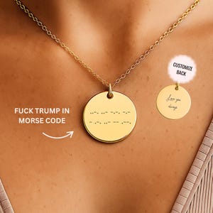 May include: Gold-colored pendant necklace with a round charm. The front of the charm has Morse code. The text "FUCK TRUMP IN MORSE CODE" is to the left of the pendant. A smaller charm on the right says "Customize Back" and has the words "Love you always".