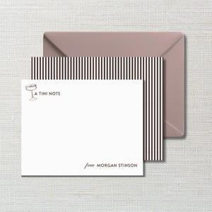 May include: A white stationery card with a black martini glass icon and the text A TINI NOTE, featuring the name MORGAN STINSON at the bottom. The card is layered over a black and white vertically striped sheet and a solid mauve envelope.