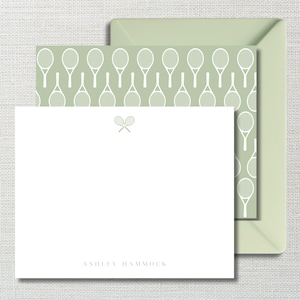 May include: A white stationery card featuring a small gray icon of two crossed tennis rackets at the top center and the name ASHLEY HAMMOCK printed in gray at the bottom, paired with a sage green envelope with a white tennis racket pattern.