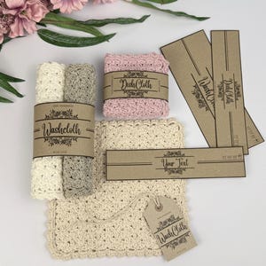Op de afbeelding: Een verzameling handgemaakte washandjes en afwasdoekjes in crème, grijs en roze, met bijpassende labels en banden. De washandjes zijn voorzien van de labels "Washcloth" en "Dish Cloth" met bloemmotieven. De labels en banden zijn gemaakt van bruin papier.