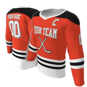 May include: An orange hockey jersey with black shoulders and white trim. The front features the text YOUR TEAM, a letter C, and crossed hockey sticks. The back displays YOUR NAME and the number 00. The sleeves have black and white stripes.