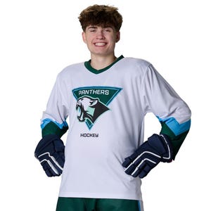 May include: A white hockey jersey with a V-neck collar, featuring a teal and dark green triangular emblem on the chest with a black panther graphic and the text PANTHERS HOCKEY. The sleeves have teal and dark green bands, paired with navy blue gloves.