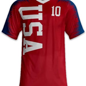 May include: Red V-neck jersey with the word "USA" in large white letters down the side and the number "10" on the upper right. The sleeves and shoulders have a blue and red design.