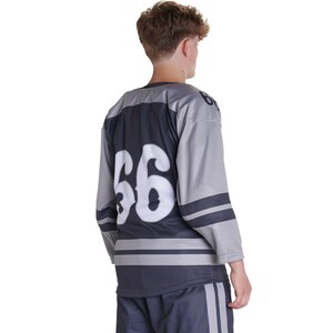 Puede incluir: Una camiseta de hockey de manga larga en color gris y azul marino oscuro con el n&uacute;mero 66 en una fuente blanca grande en la espalda. La camiseta incluye rayas horizontales azul marino oscuro en las mangas y el torso inferior, con el n&uacute;mero 66 en el hombro.
