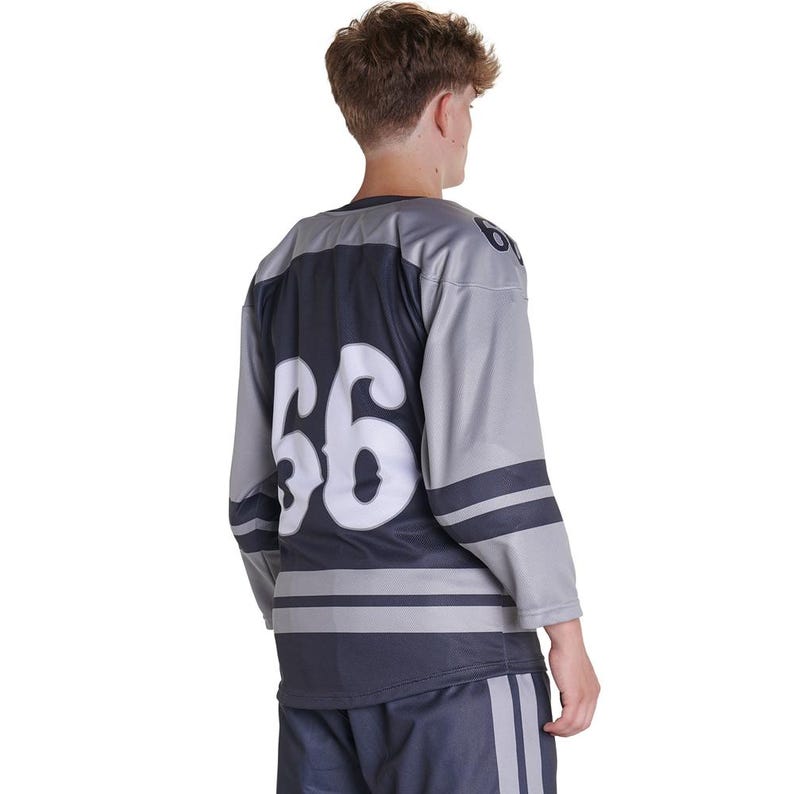 Puede incluir: Una camiseta de hockey de manga larga en color gris y azul marino oscuro con el n&uacute;mero 66 en una fuente blanca grande en la espalda. La camiseta incluye rayas horizontales azul marino oscuro en las mangas y el torso inferior, con el n&uacute;mero 66 en el hombro.