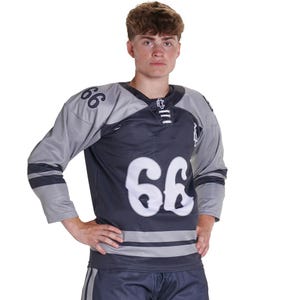 Puede incluir: Una camiseta de hockey gris oscuro y gris claro con el n&uacute;mero 66 en fuente blanca grande en el pecho y los hombros. La camiseta tiene un cuello con cordones, mangas largas con rayas horizontales oscuras y un pantal&oacute;n corto gris oscuro a juego.
