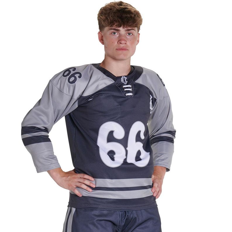 Puede incluir: Una camiseta de hockey gris oscuro y gris claro con el n&uacute;mero 66 en fuente blanca grande en el pecho y los hombros. La camiseta tiene un cuello con cordones, mangas largas con rayas horizontales oscuras y un pantal&oacute;n corto gris oscuro a juego.