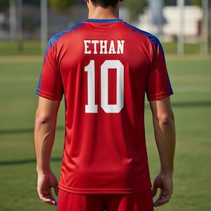 May include: Red soccer jersey with blue accents on the shoulders and collar. The name "ETHAN" and the number "10" are printed in white on the back of the jersey. The jersey is made of a lightweight, breathable material.