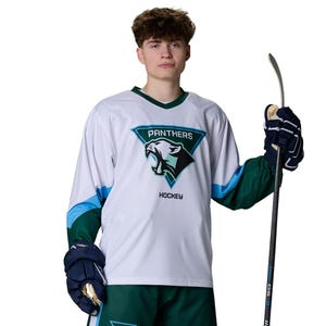 May include: A white hockey jersey with teal and dark green accents, featuring a triangular logo with a panther head and the text PANTHERS HOCKEY. The jersey has long sleeves with teal and dark green panels, paired with dark green shorts.