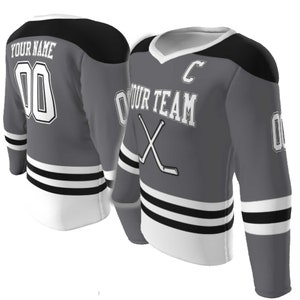May include: A grey hockey jersey with black shoulder panels and white trim. The front features the text YOUR TEAM, a letter C, and crossed hockey sticks. The back displays YOUR NAME and the number 00. Sleeves show the number 00 and black stripes.
