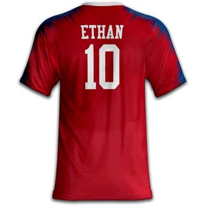 May include: Red athletic jersey with the name "ETHAN" and the number "10" in white block letters. The jersey has a white collar and blue accents on the shoulders.