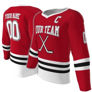 May include: A red hockey jersey featuring white and black horizontal stripes at the hem and sleeves. The front displays the text YOUR TEAM, a letter C, and crossed hockey sticks. The back shows the text YOUR NAME and the number 00 in white.