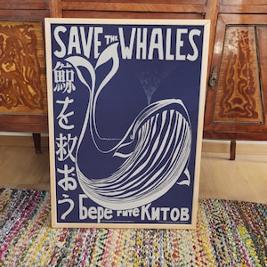 May include: A blue and white poster with the text "Save the Whales" in white lettering. The poster features a stylized illustration of a whale with Japanese text on the left side and Russian text on the bottom.