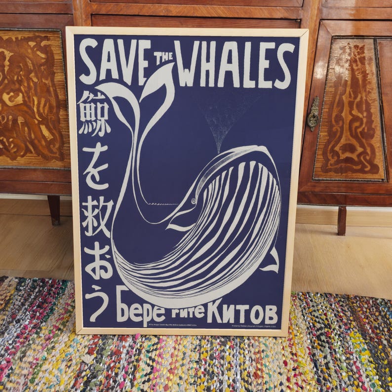 May include: A blue and white poster with the text "Save the Whales" in white lettering. The poster features a stylized illustration of a whale with Japanese text on the left side and Russian text on the bottom.