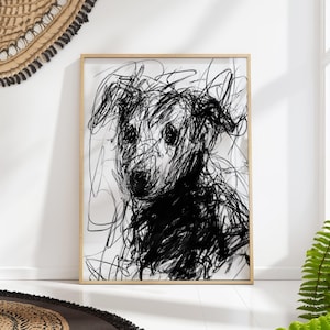 May include: Black and white abstract art print of a dog. The artwork features a sketch-like style with bold, scribbled lines creating the dog's form. The dog's face is centered, with large, expressive eyes. The print is framed in a light wood frame.