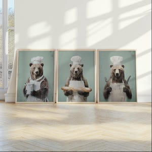 May include: Set of three framed art prints featuring anthropomorphic bears in chef attire. Each bear wears a white apron and chef's hat, holding a pot, a baguette, and a knife and fork, respectively. The background is a muted teal.