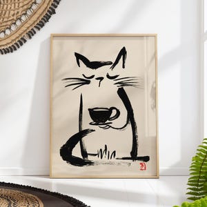 May include: A framed wall art print featuring a black ink brush stroke illustration of a cat with closed eyes holding a small cup. The cat is depicted on a light beige background with a small red stamp in the bottom right corner of the artwork.