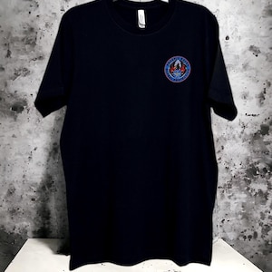 Black: Premium Poly-Cotton Blend – Soft, breathable, and durable for all-day comfort. DTF Transfer Embellishment   Features the iconic Phoenix Raven emblem on the chest and bold “RAVEN” lettering on the back using high-quality direct-to-film transfer.  Available in multiple sizes to ensure the perfect fit  Care Instructions: To preserve the design and integrity of the garment, machine wash inside out in cold water. Tumble dry on low or hang to dry. Avoid ironing directly over the graphic.