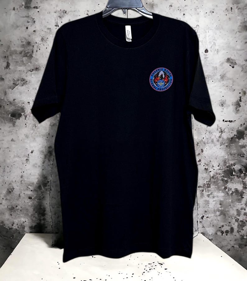 Black: Premium Poly-Cotton Blend – Soft, breathable, and durable for all-day comfort. DTF Transfer Embellishment   Features the iconic Phoenix Raven emblem on the chest and bold “RAVEN” lettering on the back using high-quality direct-to-film transfer.  Available in multiple sizes to ensure the perfect fit  Care Instructions: To preserve the design and integrity of the garment, machine wash inside out in cold water. Tumble dry on low or hang to dry. Avoid ironing directly over the graphic.