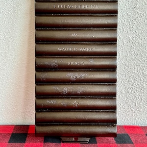 May include: Vintage cast iron bread stick pan with the text "E BREAD STICK PAN", "W", "WAGNER WARE", "SIDNEY", and "OHIO" embossed on the front. The pan has a star shape embossed on the bottom.