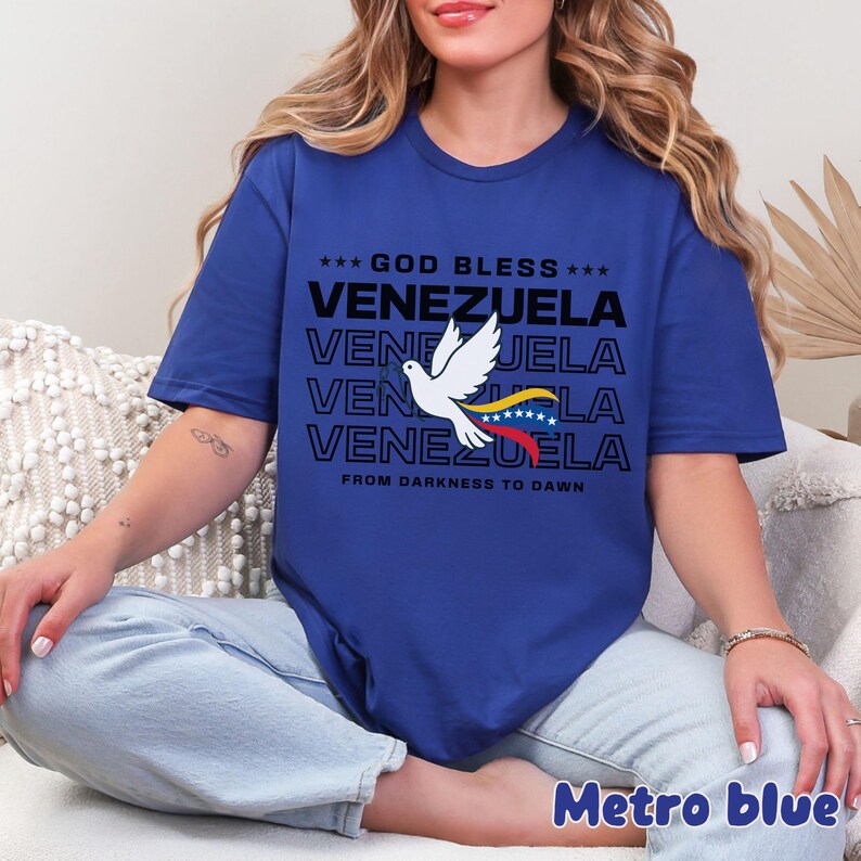 May include: Metro blue t-shirt with the text "GOD BLESS VENEZUELA" and a dove carrying the Venezuelan flag. The shirt also includes the phrase "FROM DARKNESS TO DAWN".