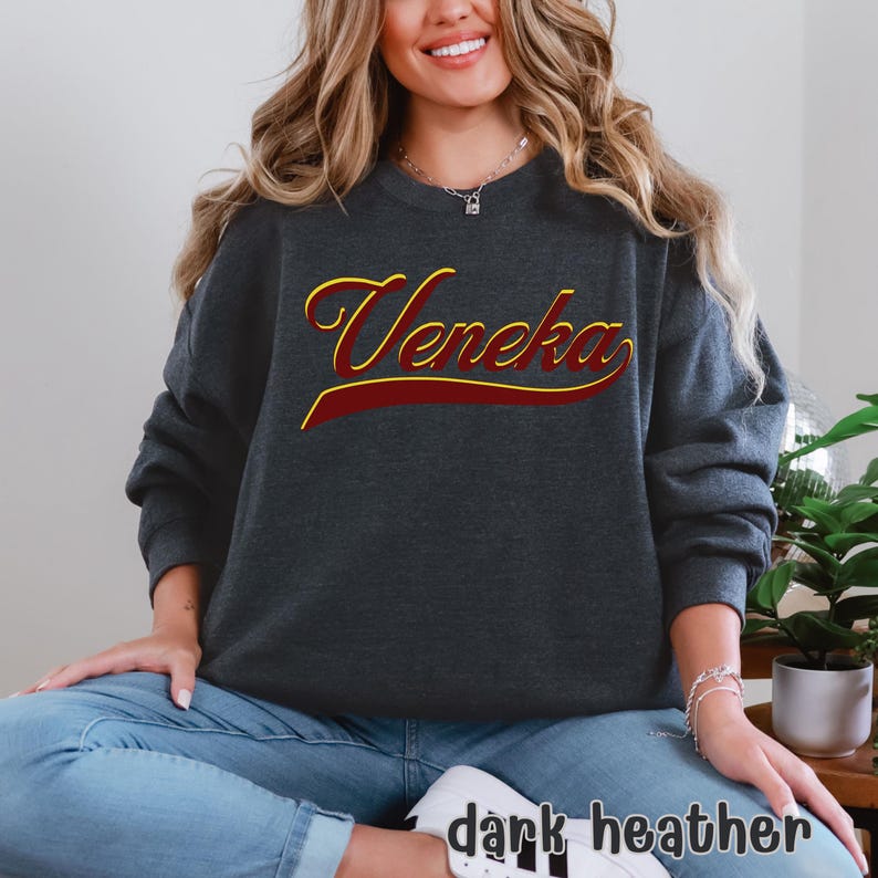 A person wearing a dark heather grey crewneck sweatshirt with "Veneka" in red and yellow script across the chest, with "dark heather" written in white in the bottom right corner.