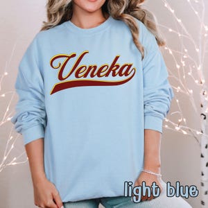 A person wearing a light blue crewneck sweatshirt with "Veneka" in red and yellow script across the chest, with "light blue" written in white in the bottom right corner.