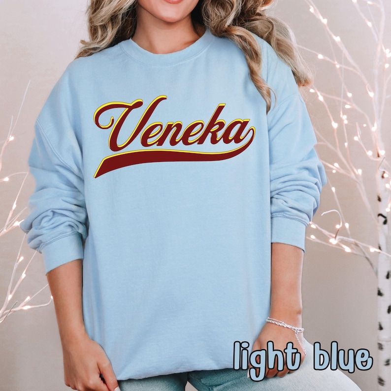 A person wearing a light blue crewneck sweatshirt with "Veneka" in red and yellow script across the chest, with "light blue" written in white in the bottom right corner.