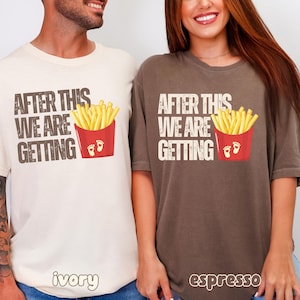 Op de afbeelding: Een ivoorkleurig t-shirt en een espresso-kleurig t-shirt, beide met de tekst "AFTER THIS WE ARE GETTING" boven een afbeelding van een rode kartonnen doos gevuld met gele frietjes, met twee kleine witte babyvoetjes op de doos.