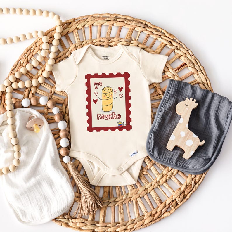 May include: Cream-colored baby onesie with a red postage stamp design featuring a cartoon roll with hearts and the words "yo mucho". A wooden giraffe, a gray burp cloth, and a pacifier are also in the image.