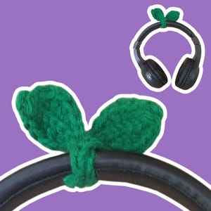 May include: Black headphones with green knitted ear covers. The ear covers are shaped like leaves and are attached to the headphones with a knot.