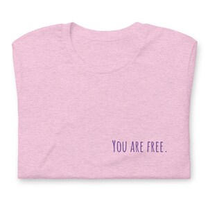 May include: A pink heather t-shirt with the text "YOU ARE FREE." printed in purple on the bottom right corner.